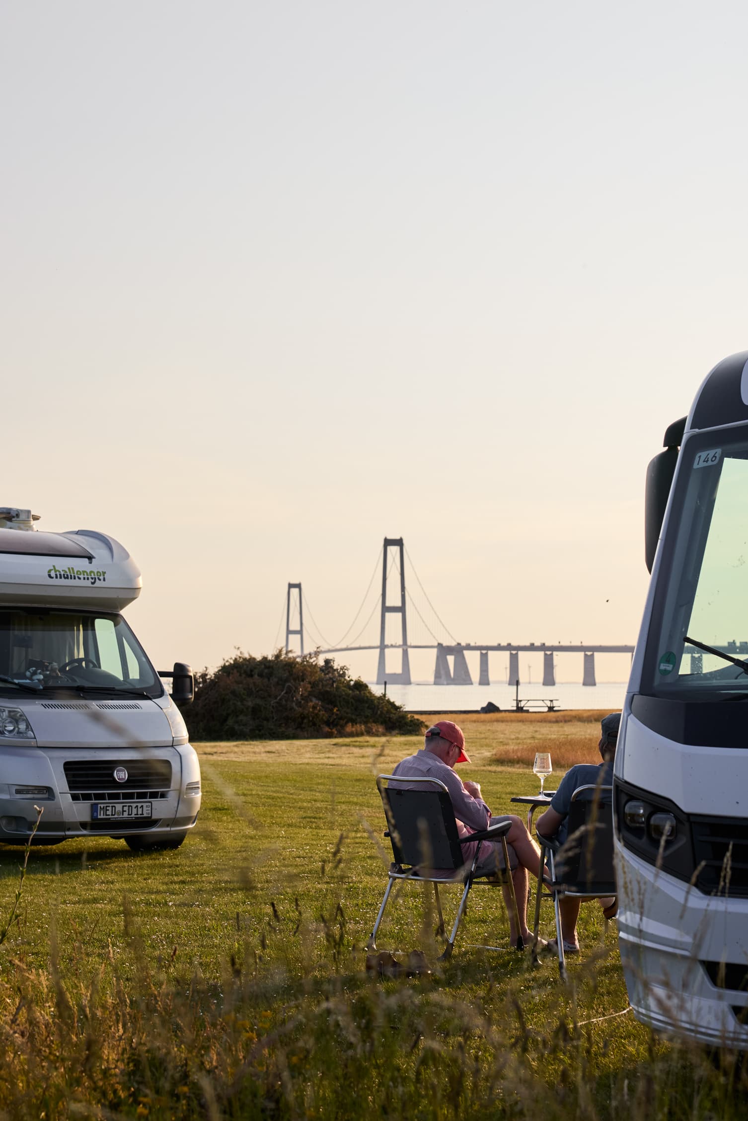 Autocamperpar nyder solnedgang ved Storebælt Camping med udsigt mod Storebæltsbroen
